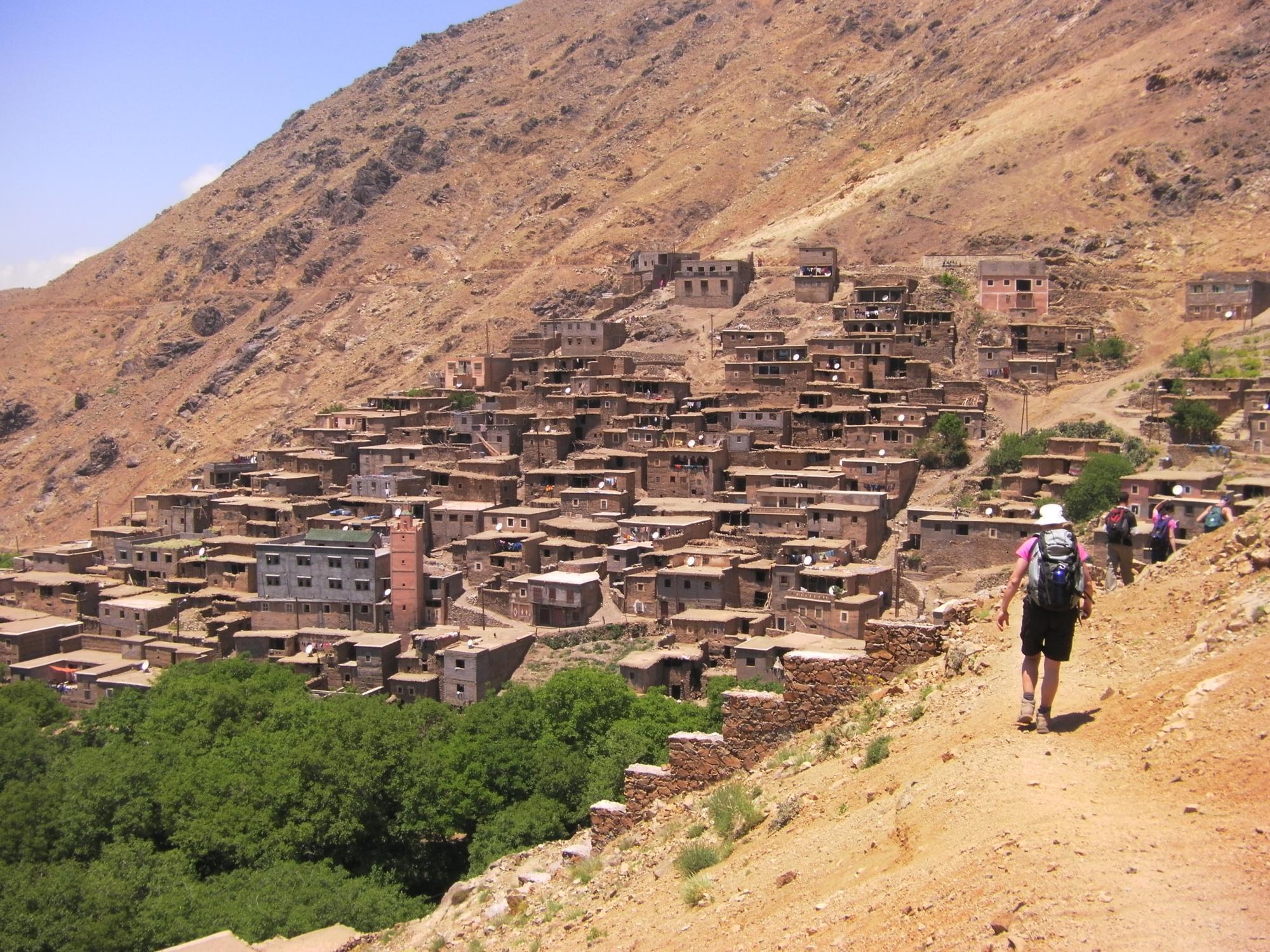 Hikers descending toward an Atlas Mountains village